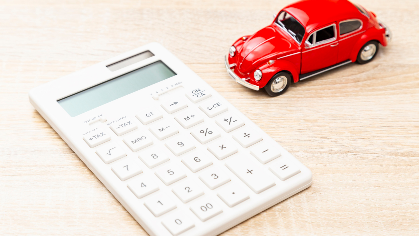 White calculator next to a small red toy car on a light-colored wooden surface.