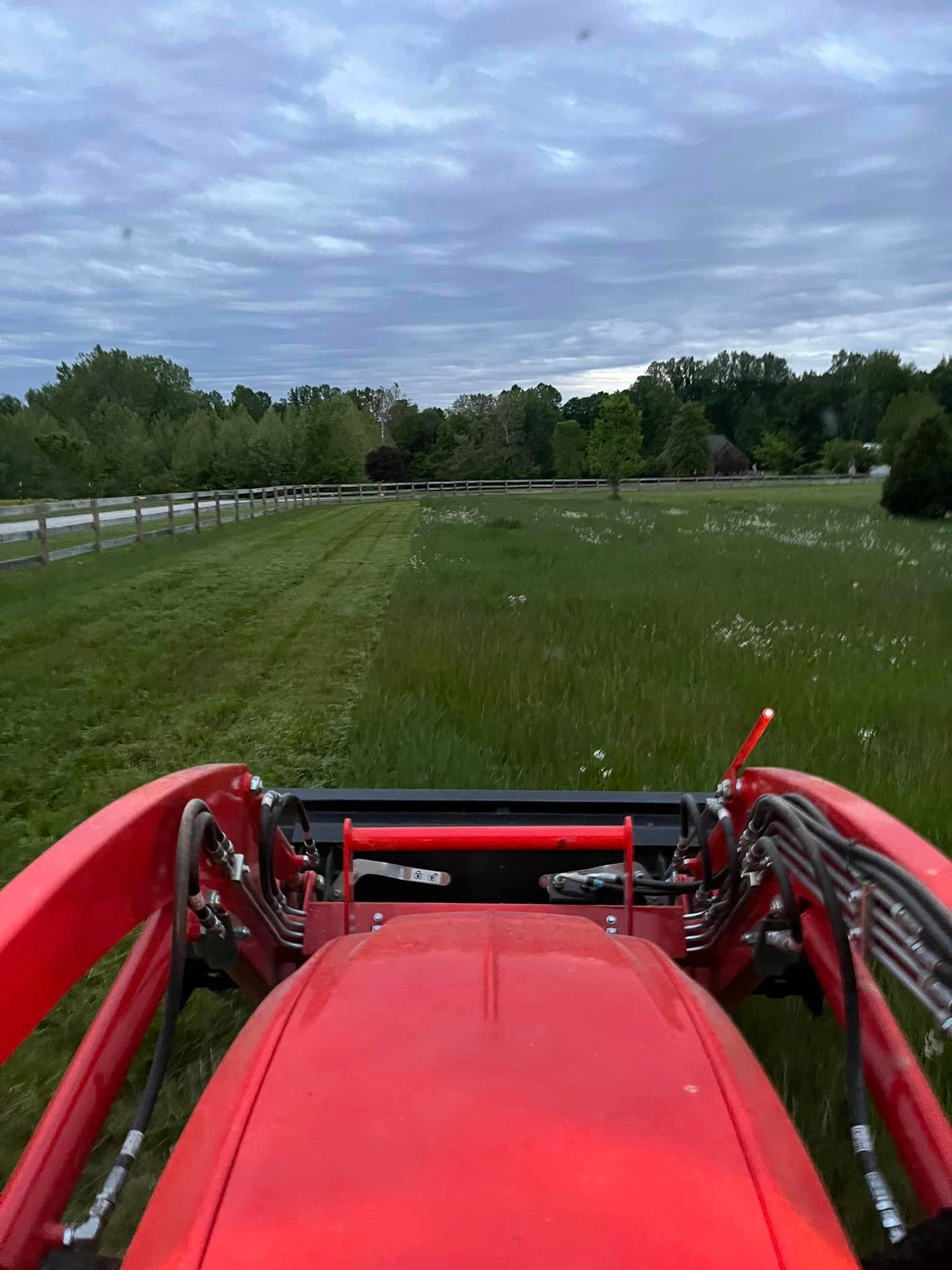 a red tractor is driving through a grassy field .