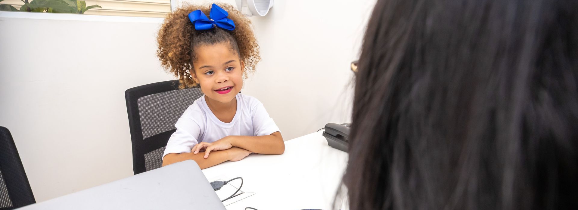 Uma menina está sentada à mesa conversando com uma mulher.