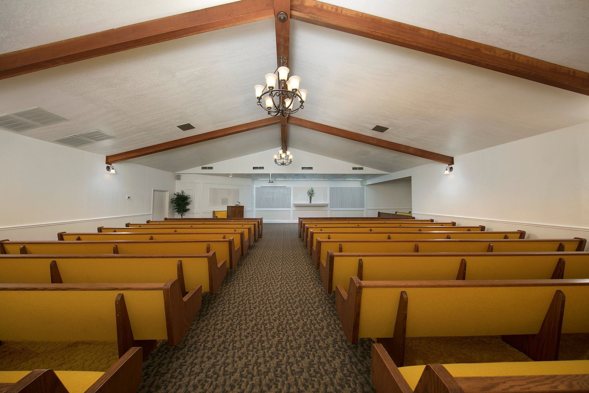 An empty church with yellow benches and a chandelier hanging from the ceiling.