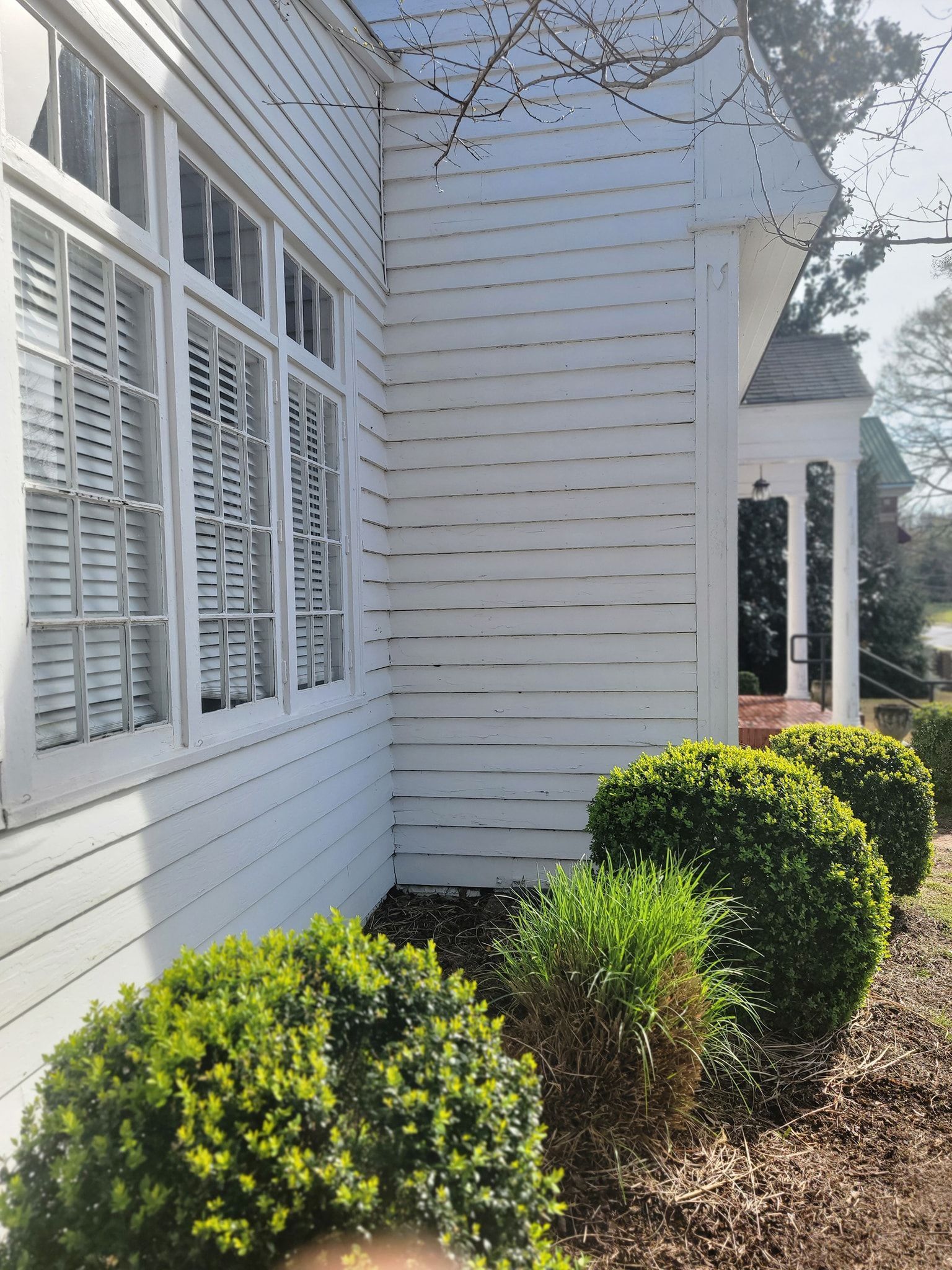 White clapboard house with shutters, manicured bushes in front.