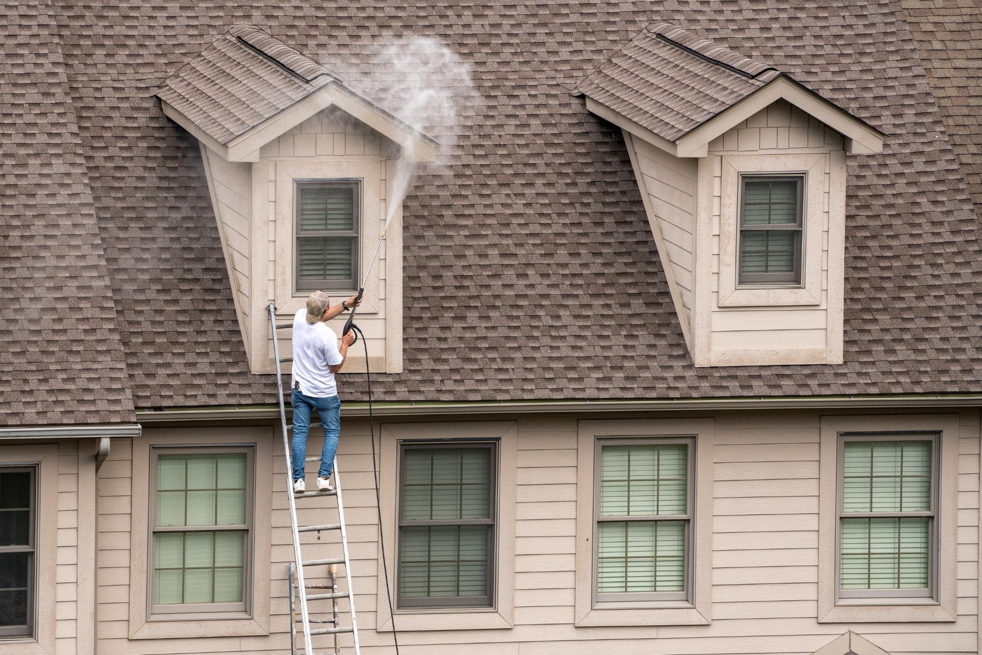 Man pressure washing a dormer window on a two-story house.