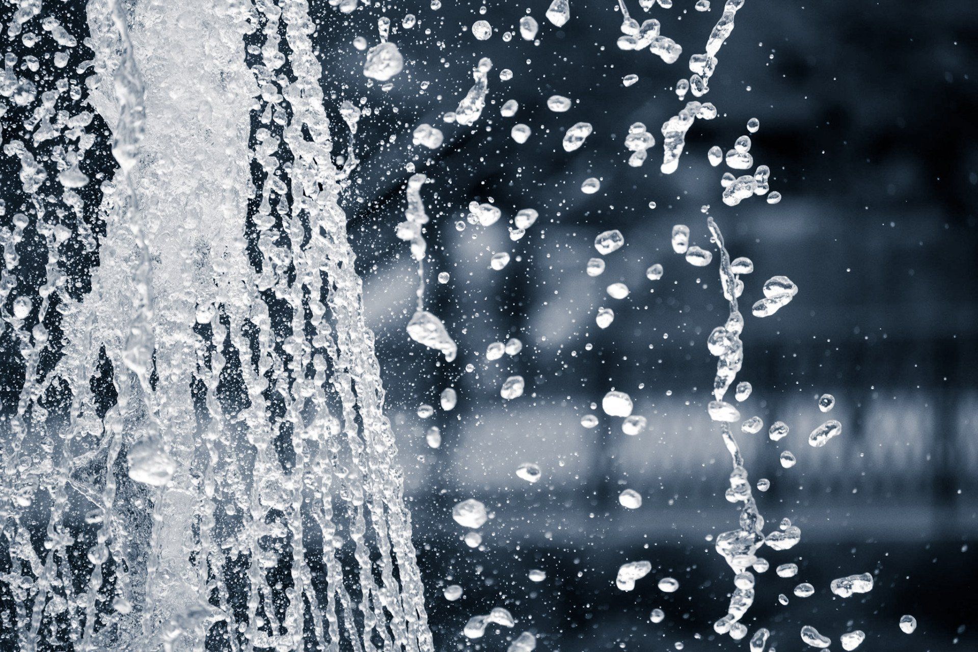 Close-up of water fountain with water droplets splashing, against a dark background.