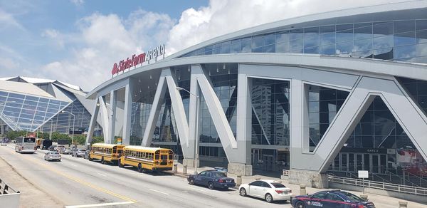 State Farm Arena exterior with school buses, cars, and a cloudy sky.