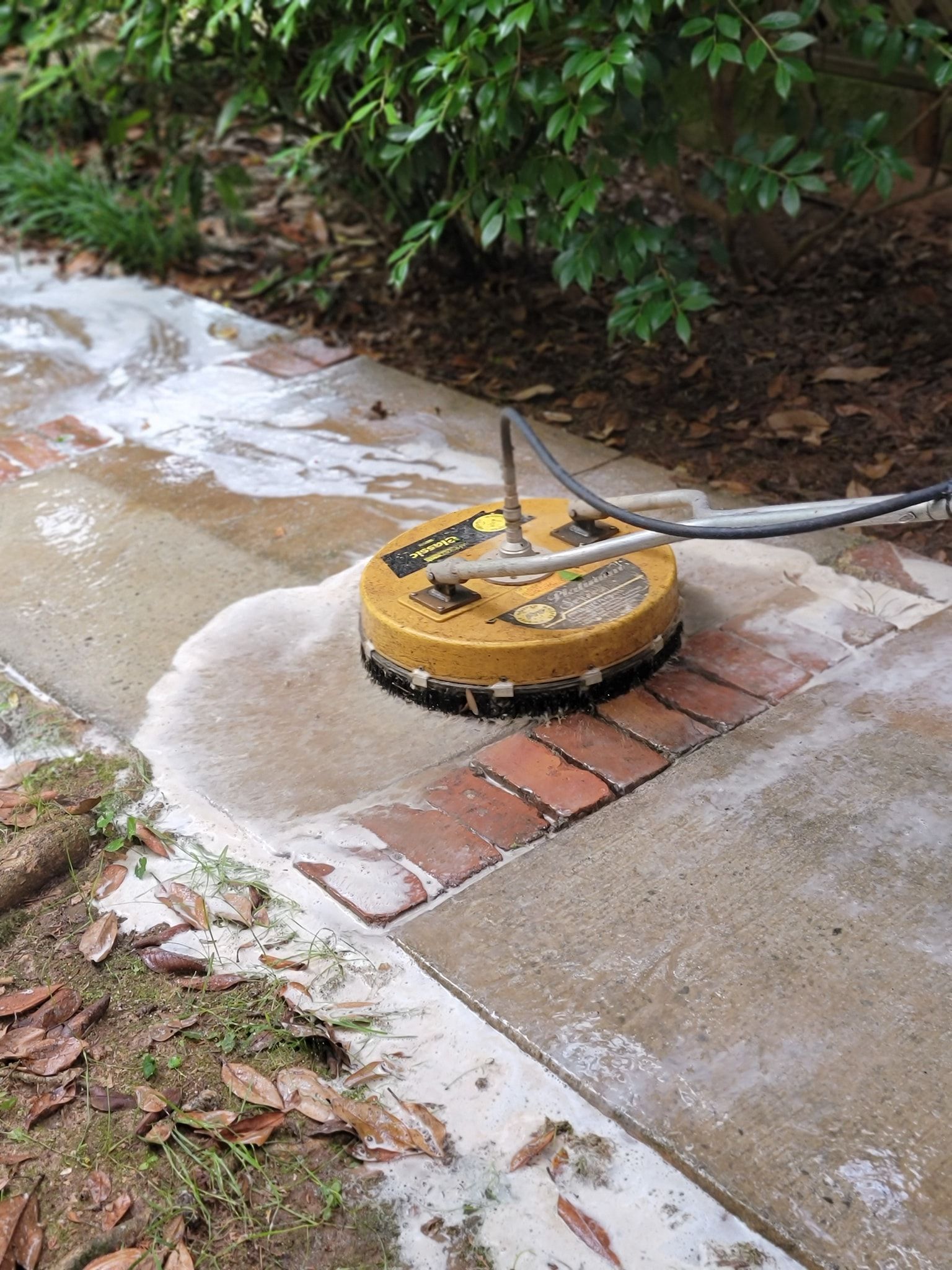 Pressure washer cleaning a concrete walkway and brick border.