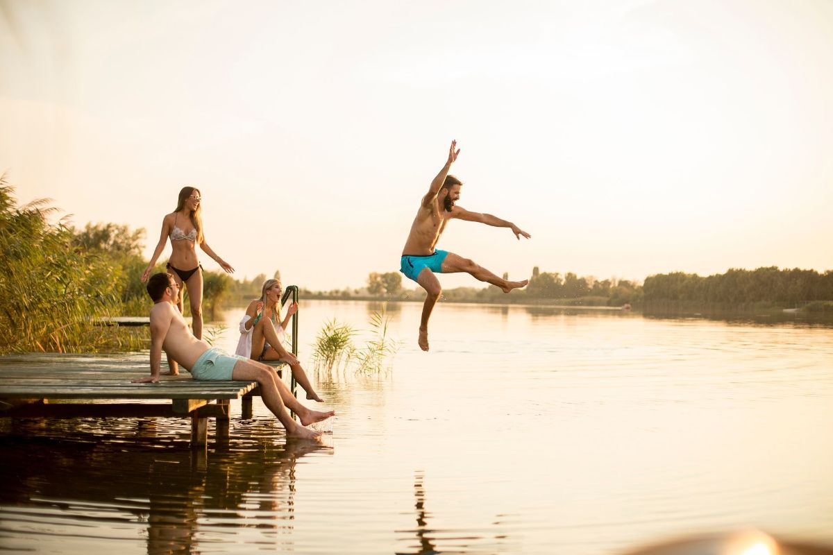 A group of people are jumping into a lake from a dock.