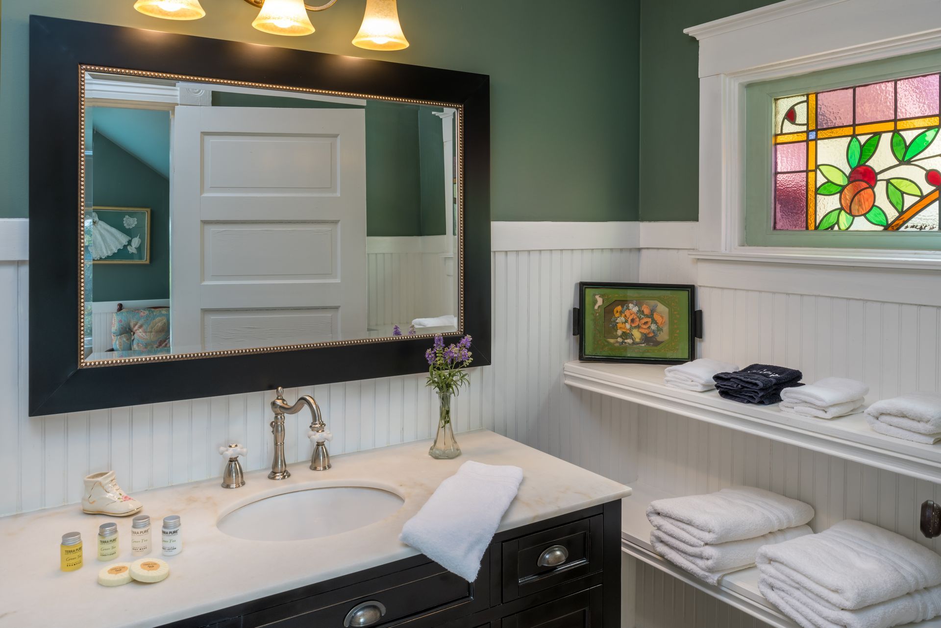 A bathroom with a sink , mirror and stained glass window.