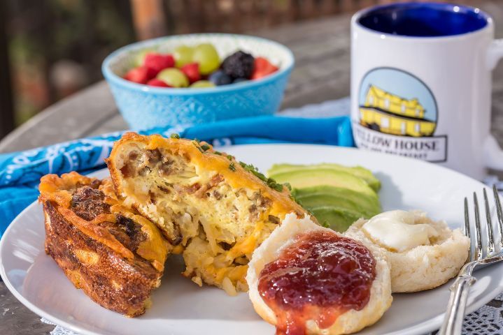 A plate of food with a cup of coffee and a bowl of fruit on a table.