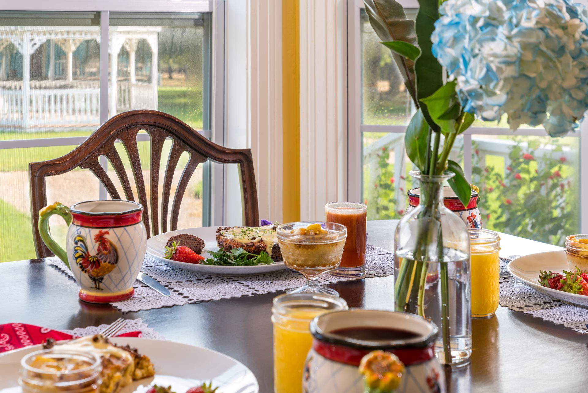 A table with plates of food and drinks on it in front of a window.