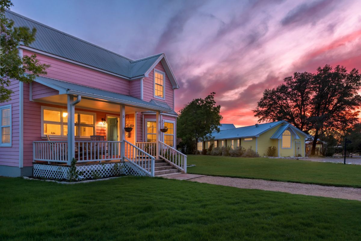 A pink house with a blue roof and a porch at sunset.