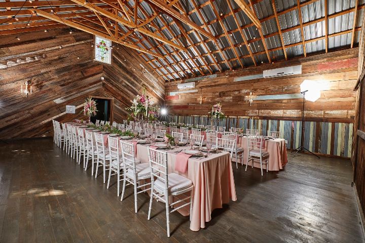 A long table and chairs are set up in a barn for a wedding reception.