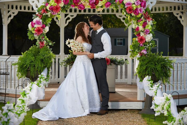 A bride and groom are kissing in front of a gazebo decorated with flowers.