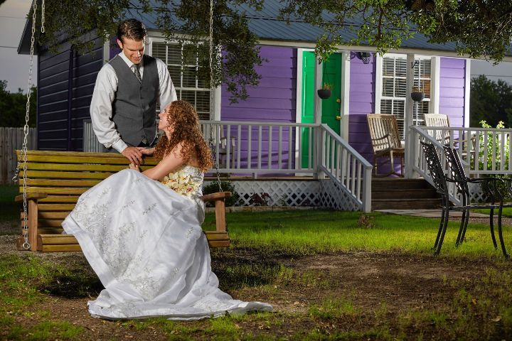 A bride and groom are sitting on a swing in front of a purple house.