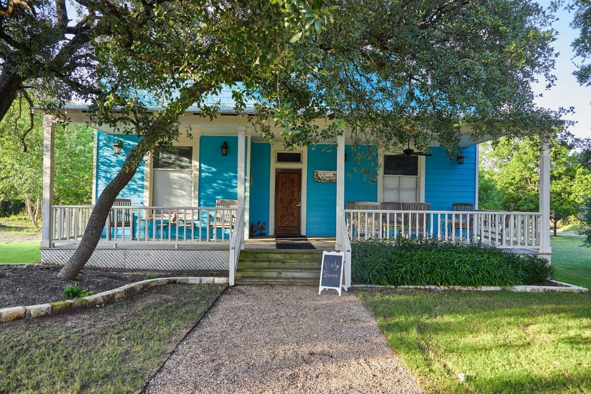 A blue house with a white porch and a sign in front of it.