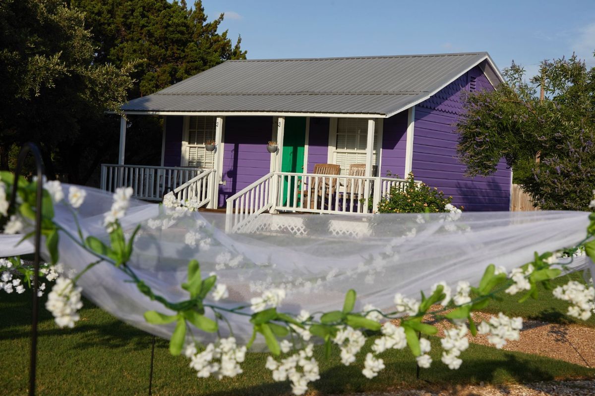 A purple house with a green door is surrounded by white flowers.