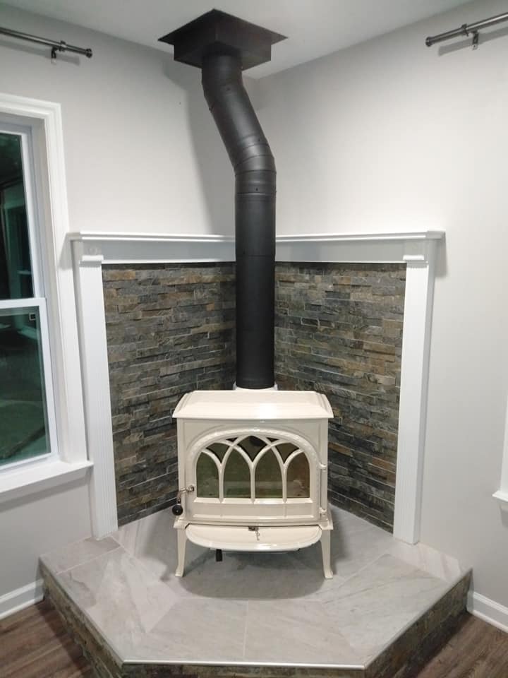A wood stove is sitting in the corner of a living room next to a window.