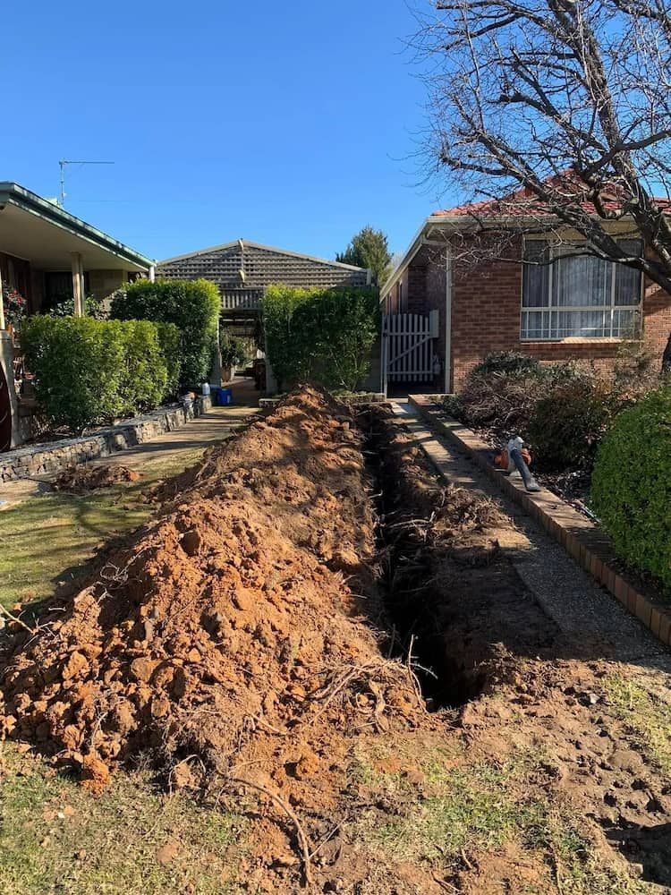 A Trench Dug in a Front Yard With Dirt Piled — Riverina Tree Fellas in Cootamundra, NSW