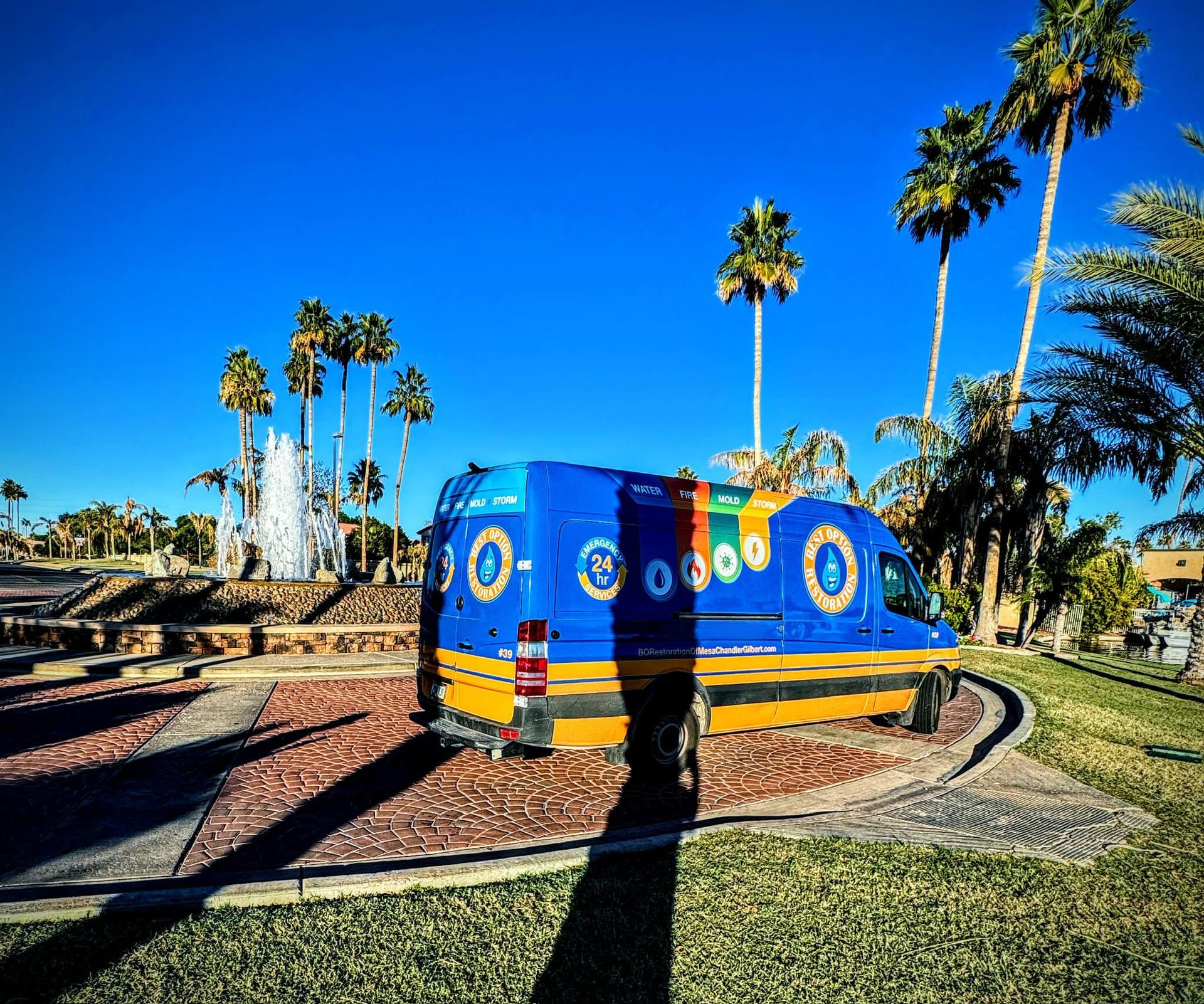 A blue and yellow van is parked in front of a fountain.