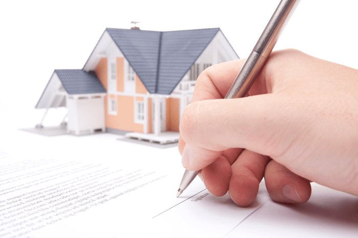 Una persona escribe en una hoja de papel frente a una casa modelo.