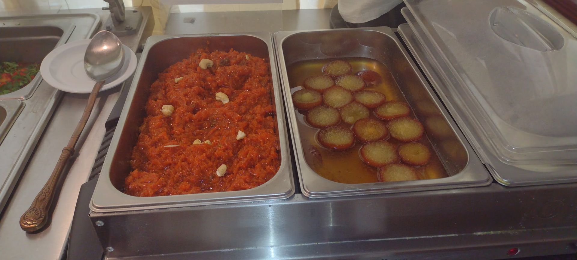 Dessert buffet: carrot halwa with cashews and gulab jamun. Stainless steel trays.