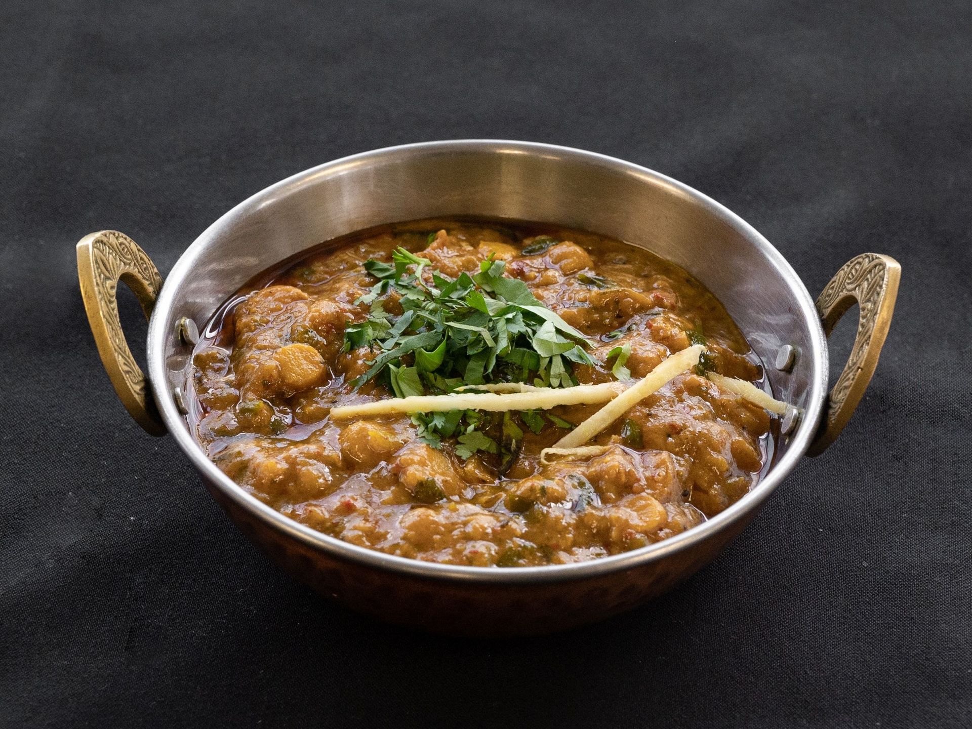 Chickpea curry in a copper bowl, garnished with cilantro and ginger.