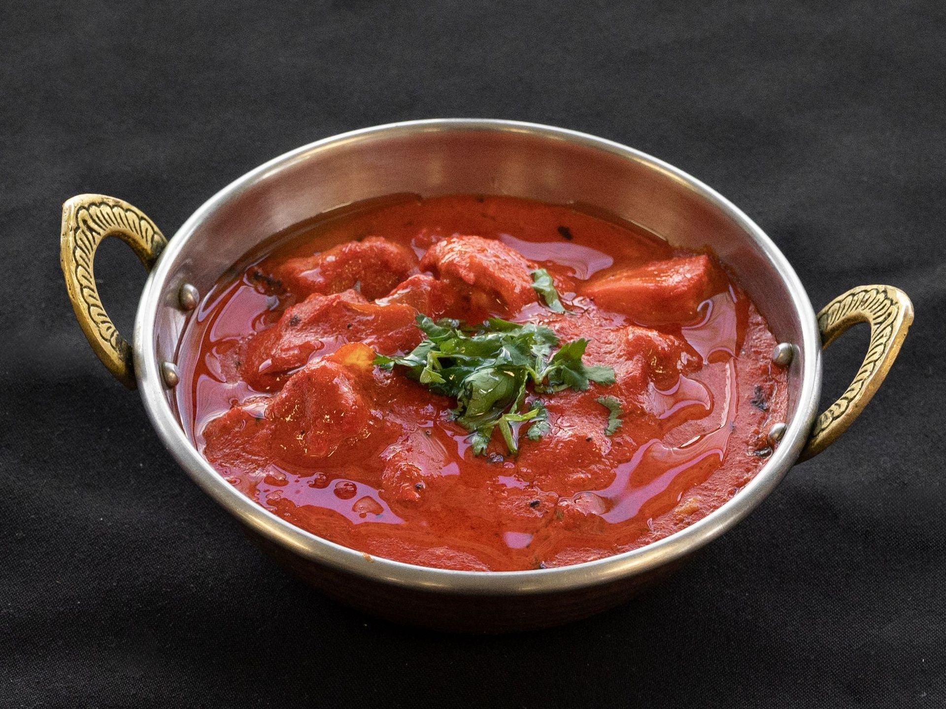 Chicken tikka masala in a copper bowl with gold handles; garnished with cilantro.