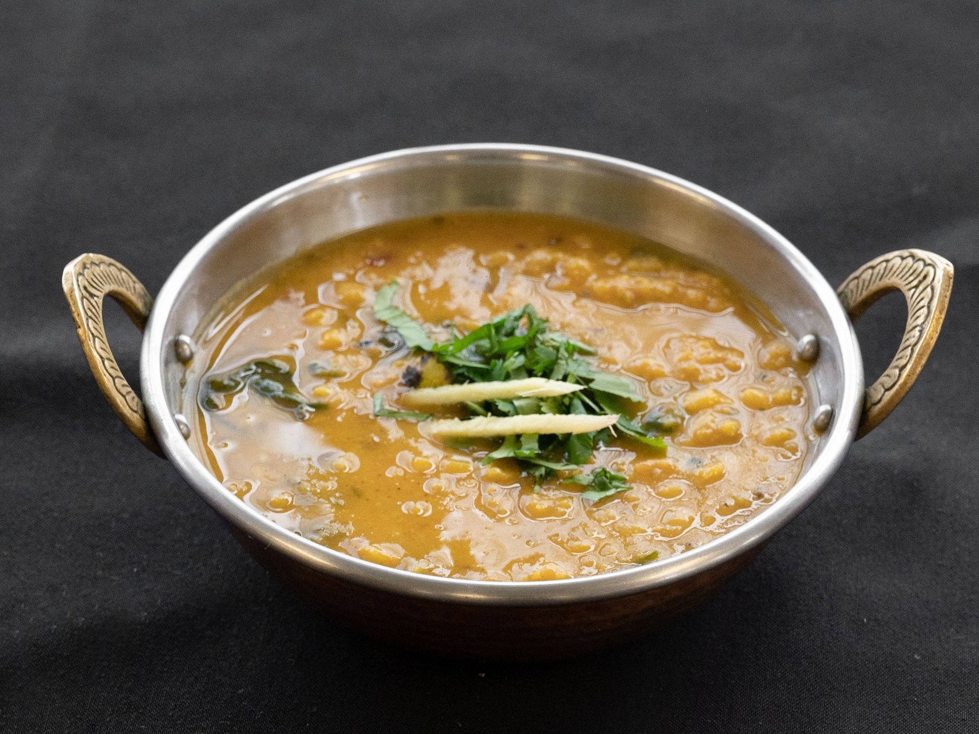 Dal in a decorative metal bowl, garnished with cilantro and ginger.