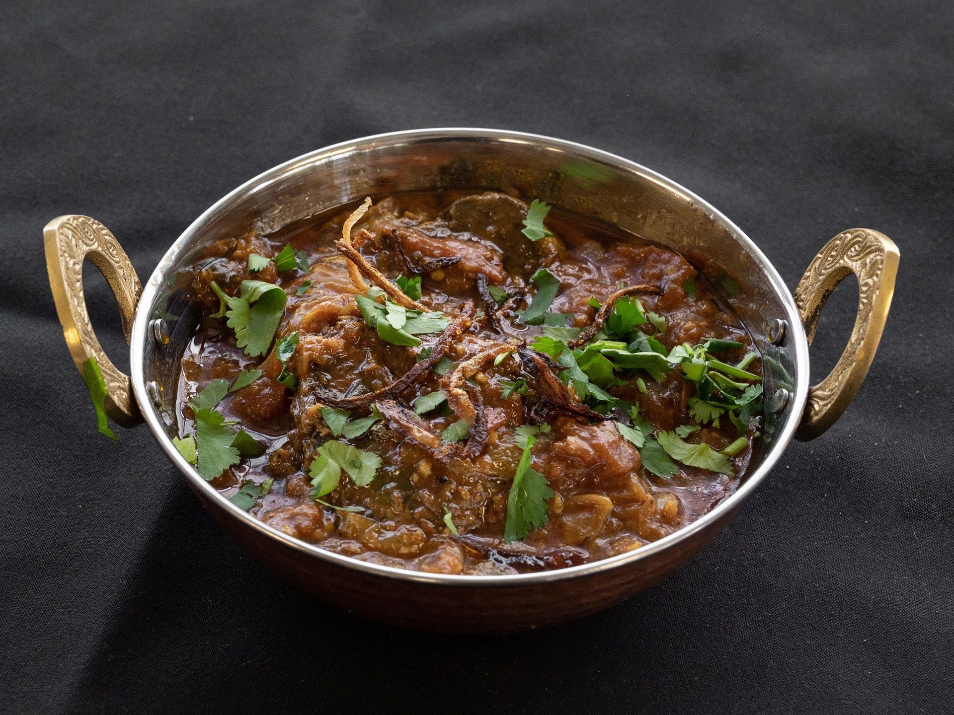 A bowl of savory curry, garnished with cilantro, against a dark backdrop.