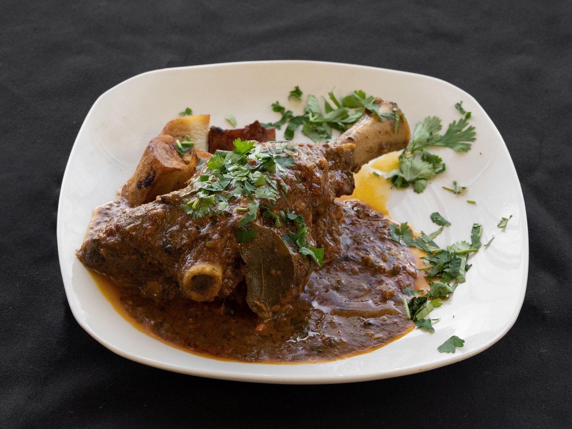 Lamb stew on a white plate, garnished with herbs.