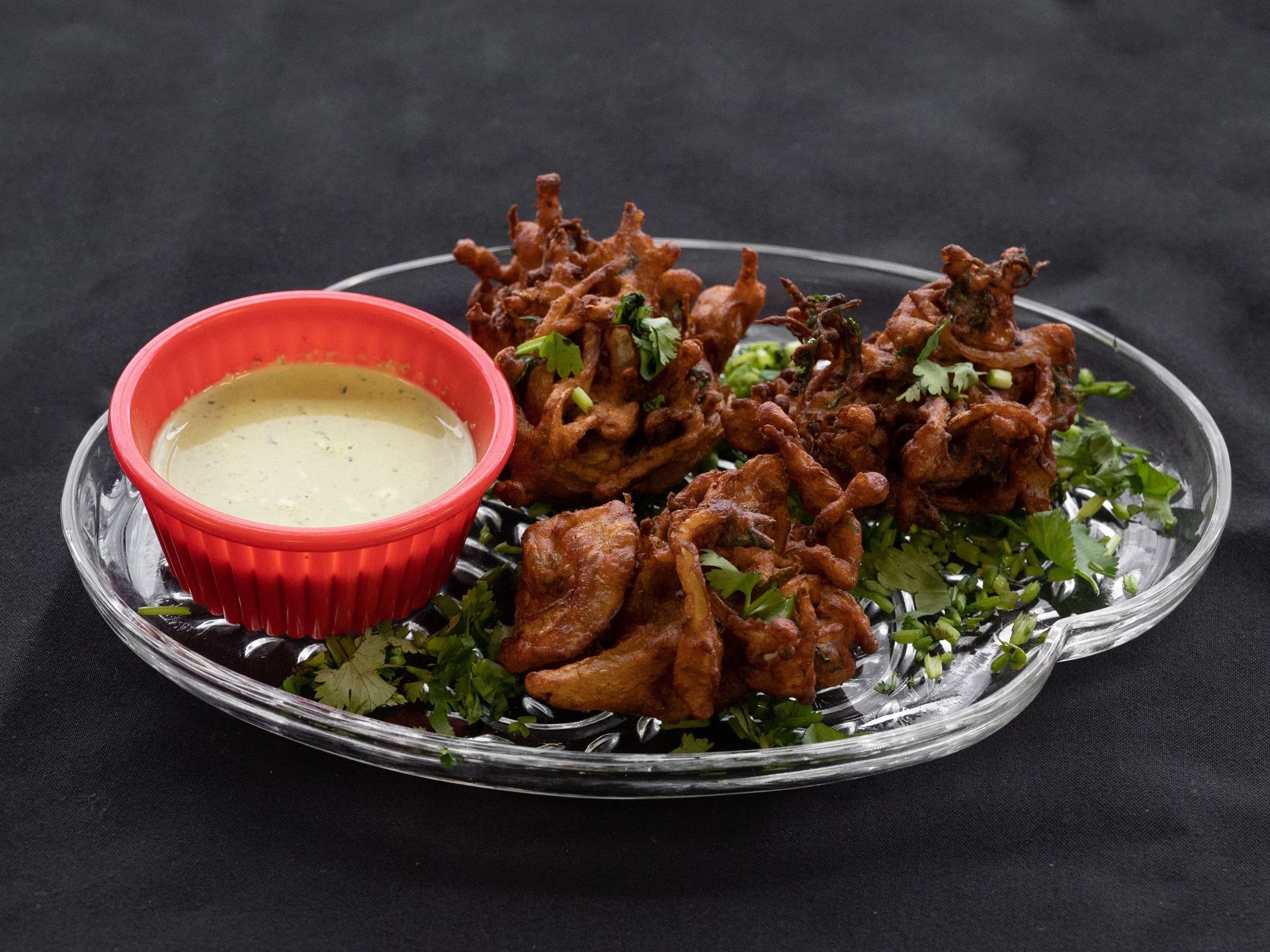Pakoras with creamy sauce on a decorative plate, garnished with cilantro.