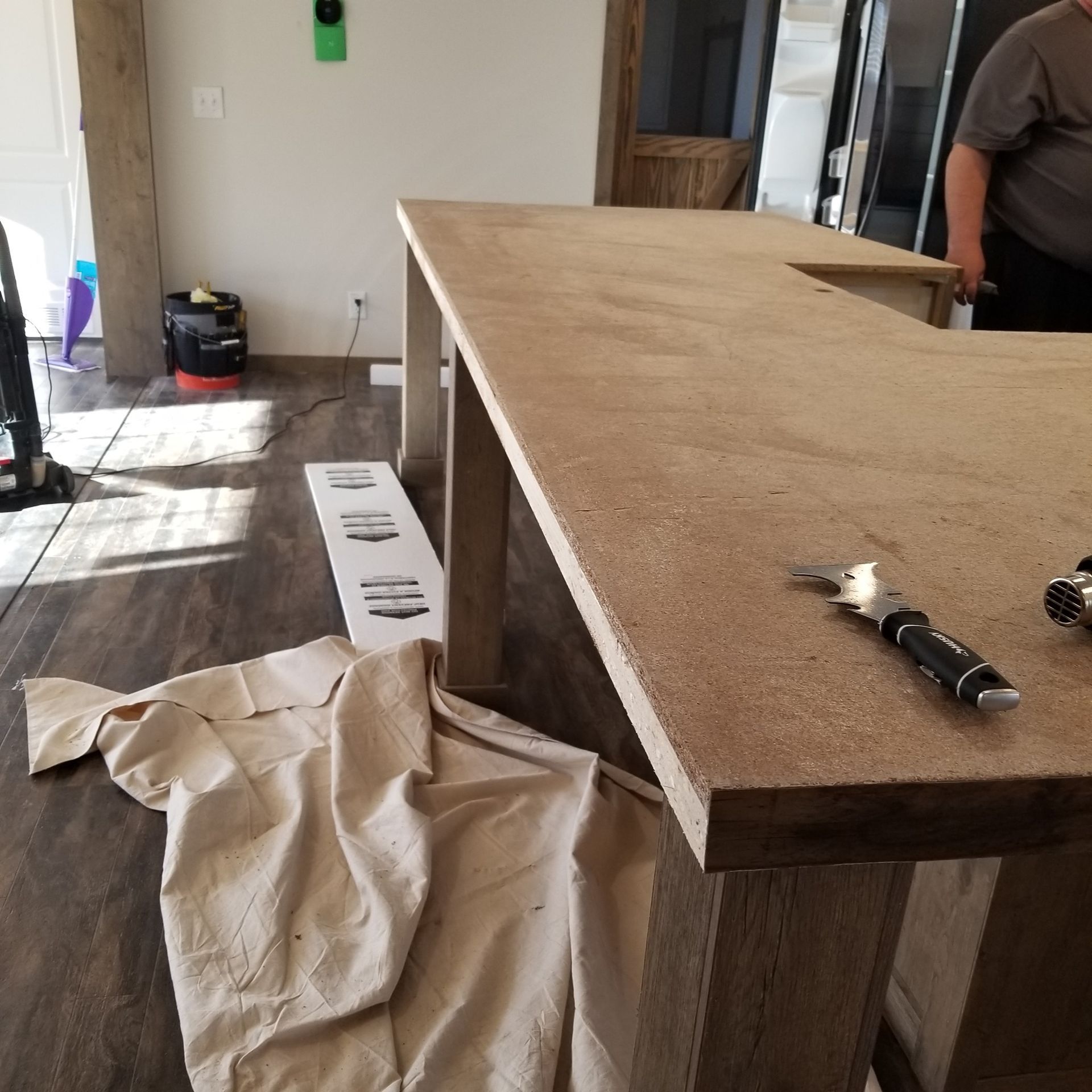 A light brown countertop with a person working on it in a room with hardwood floors.