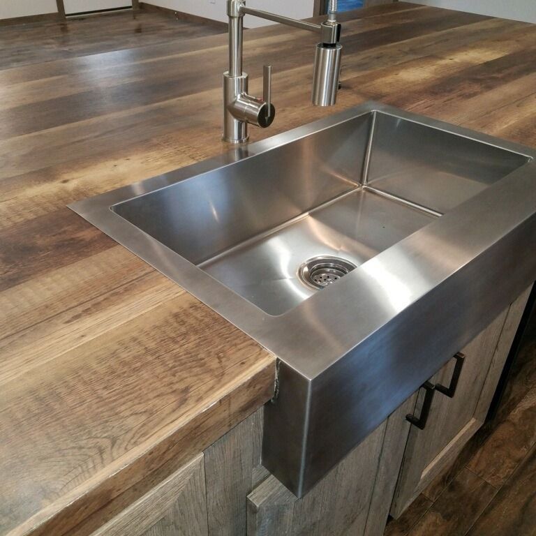 Stainless steel farmhouse sink in a wood countertop, with cabinetry below.