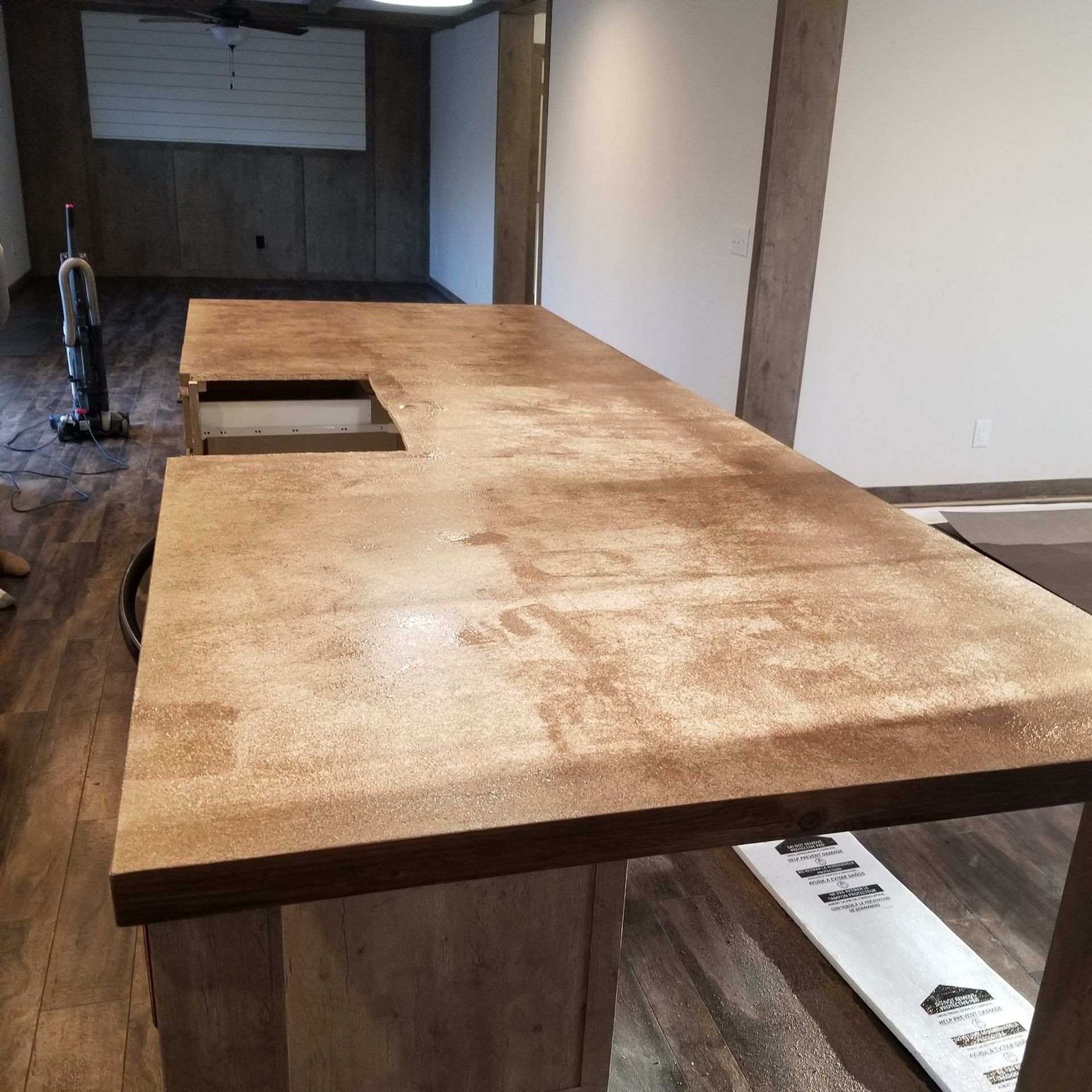 Brown countertop with a cutout, in a room with a vacuum cleaner and bare walls.