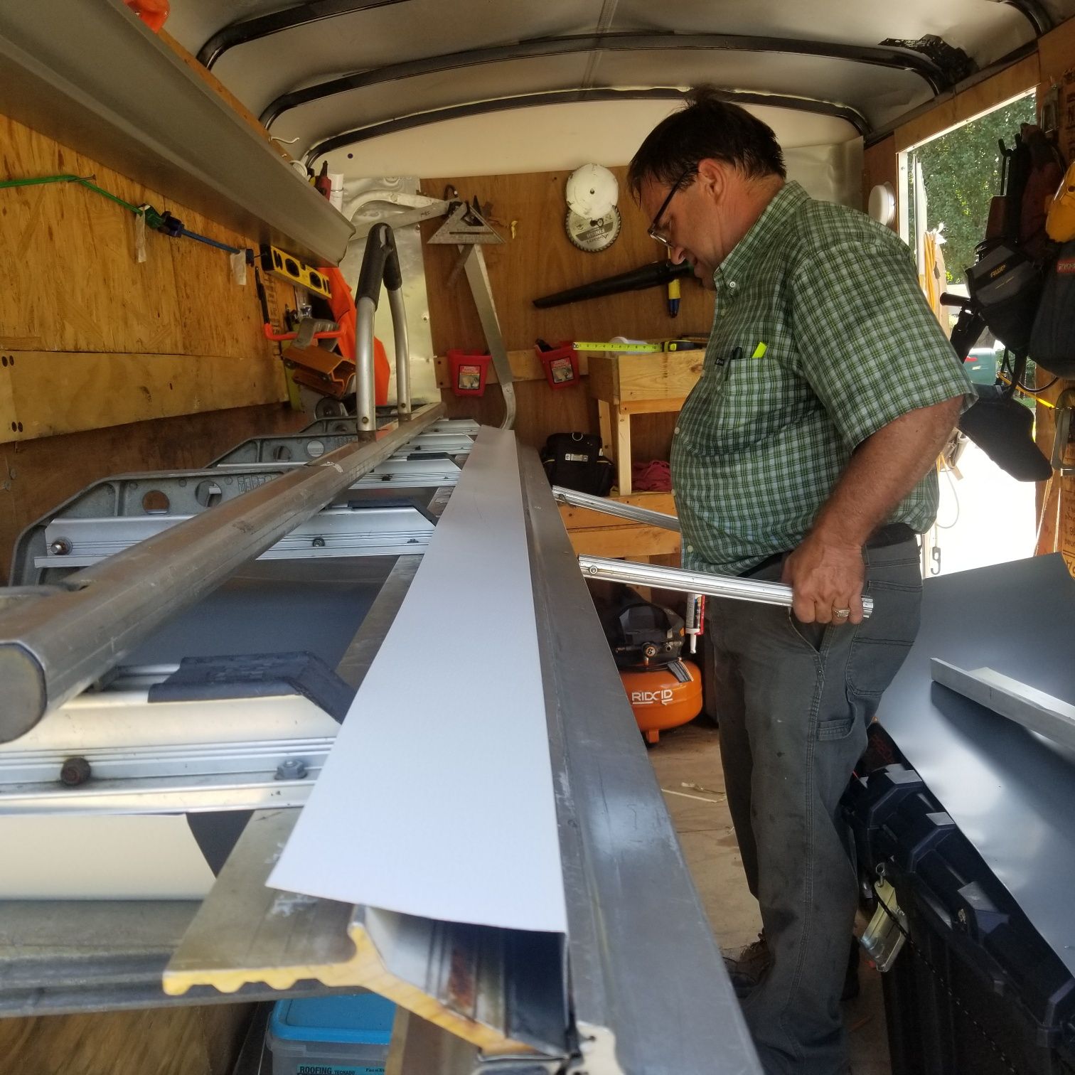 Man in a trailer using a saw. He is holding a tool and looking at a piece of light gray material.