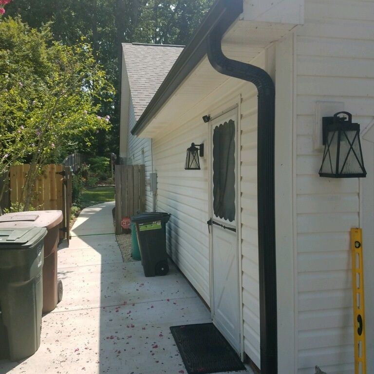 Side of a white building with black gutters, a door, and a walkway with trash cans.