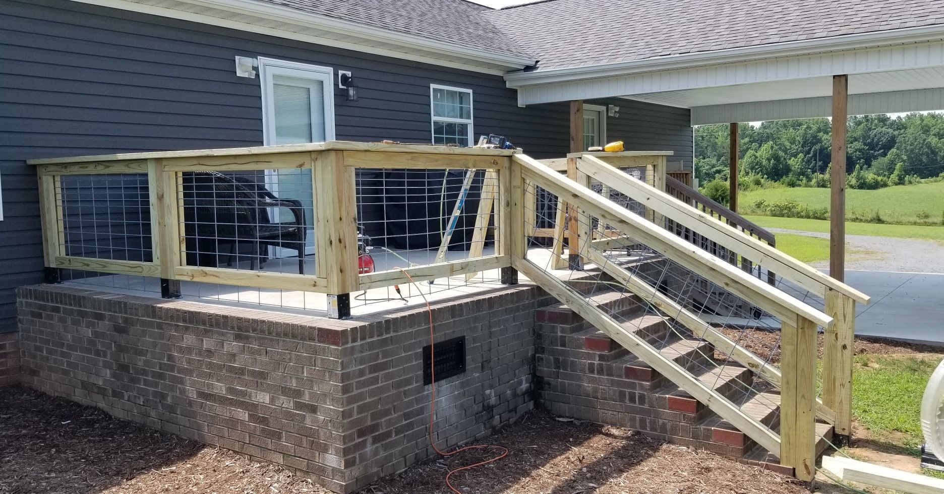 Wooden deck with stairs, brick foundation, and dark siding on a house.