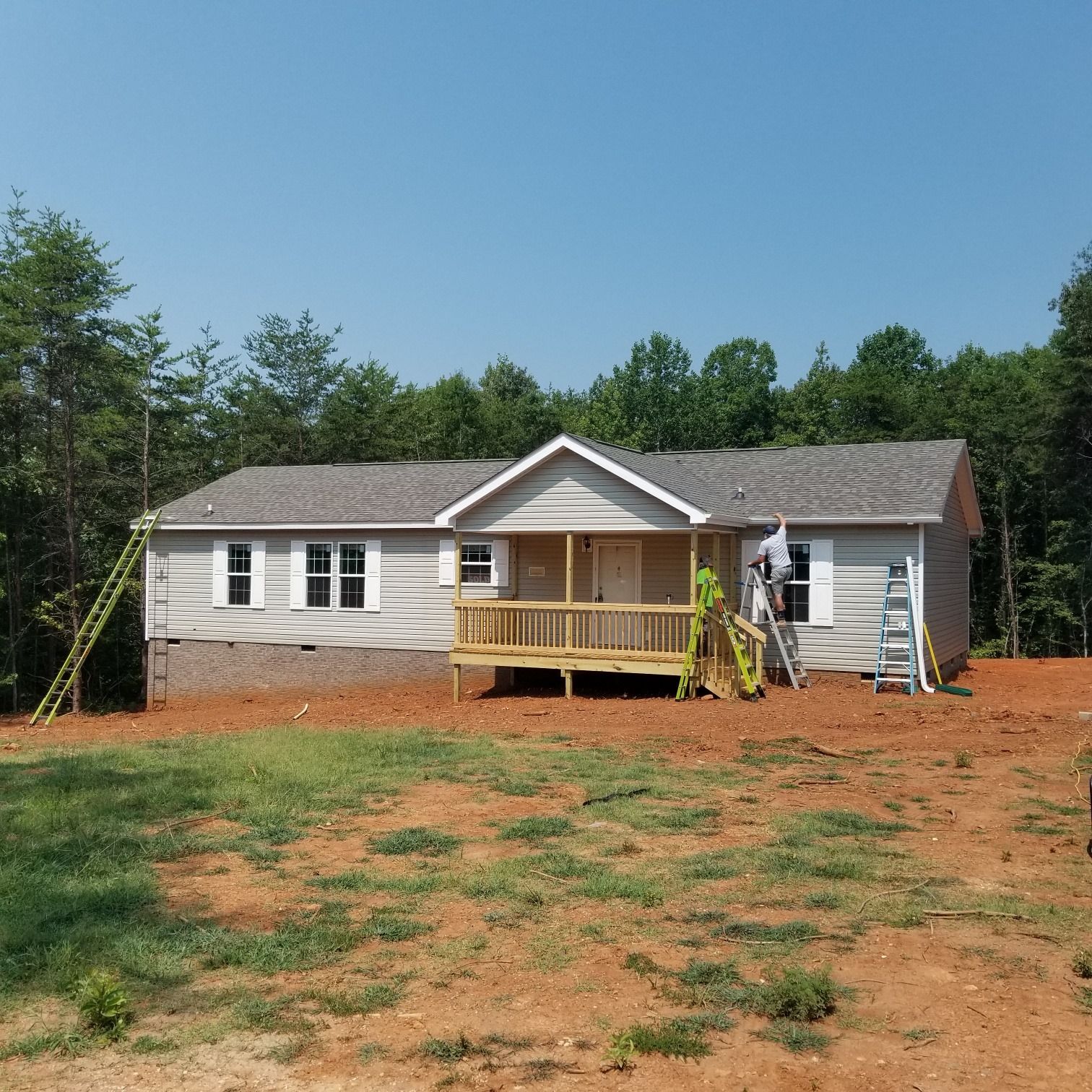 A one-story house under construction with a wooden porch and surrounding trees.