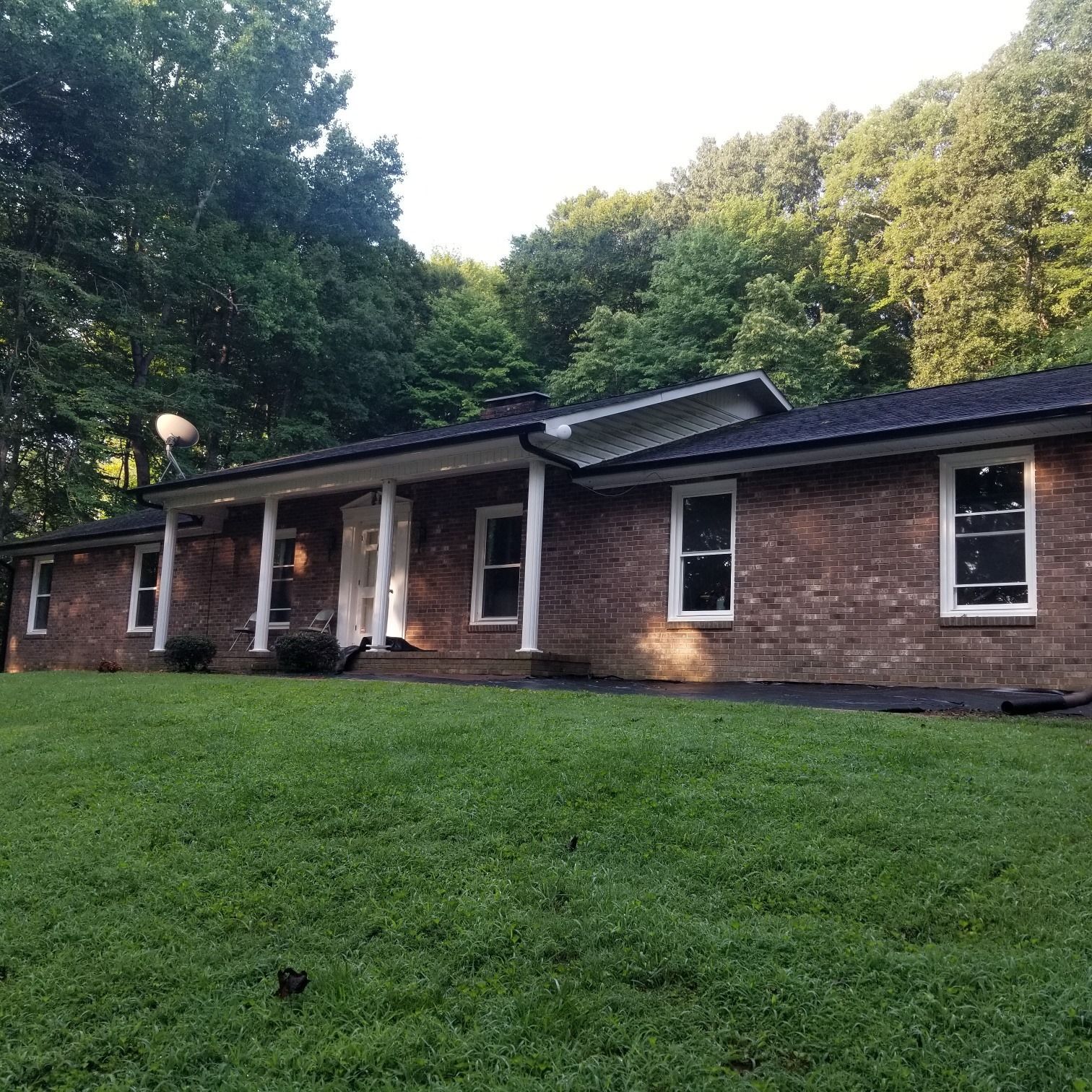 Brick house with white trim, green lawn, and trees in the background.
