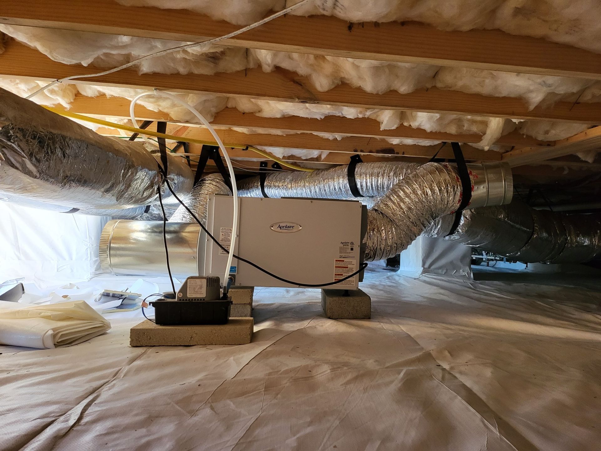 Crawlspace with a dehumidifier system, ductwork, insulation, and vapor barrier.