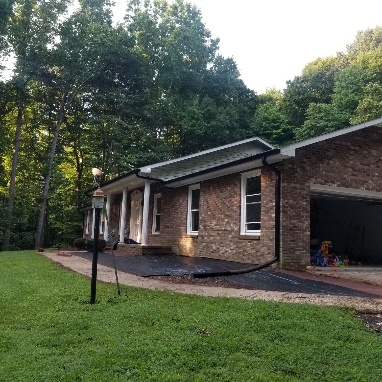 Brick house with a driveway and garage, surrounded by trees and grass.
