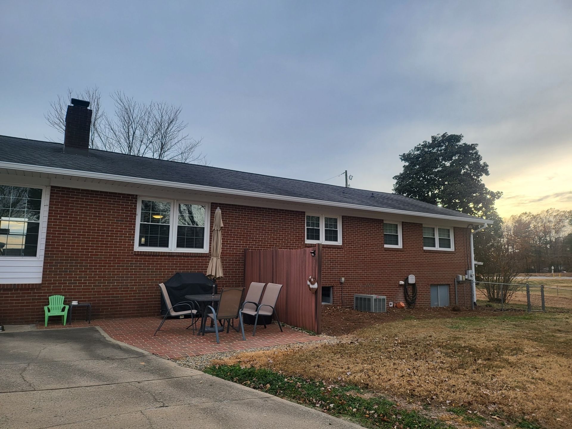 Red brick house with patio, table, chairs, and umbrella. Overcast sky, dry grass.