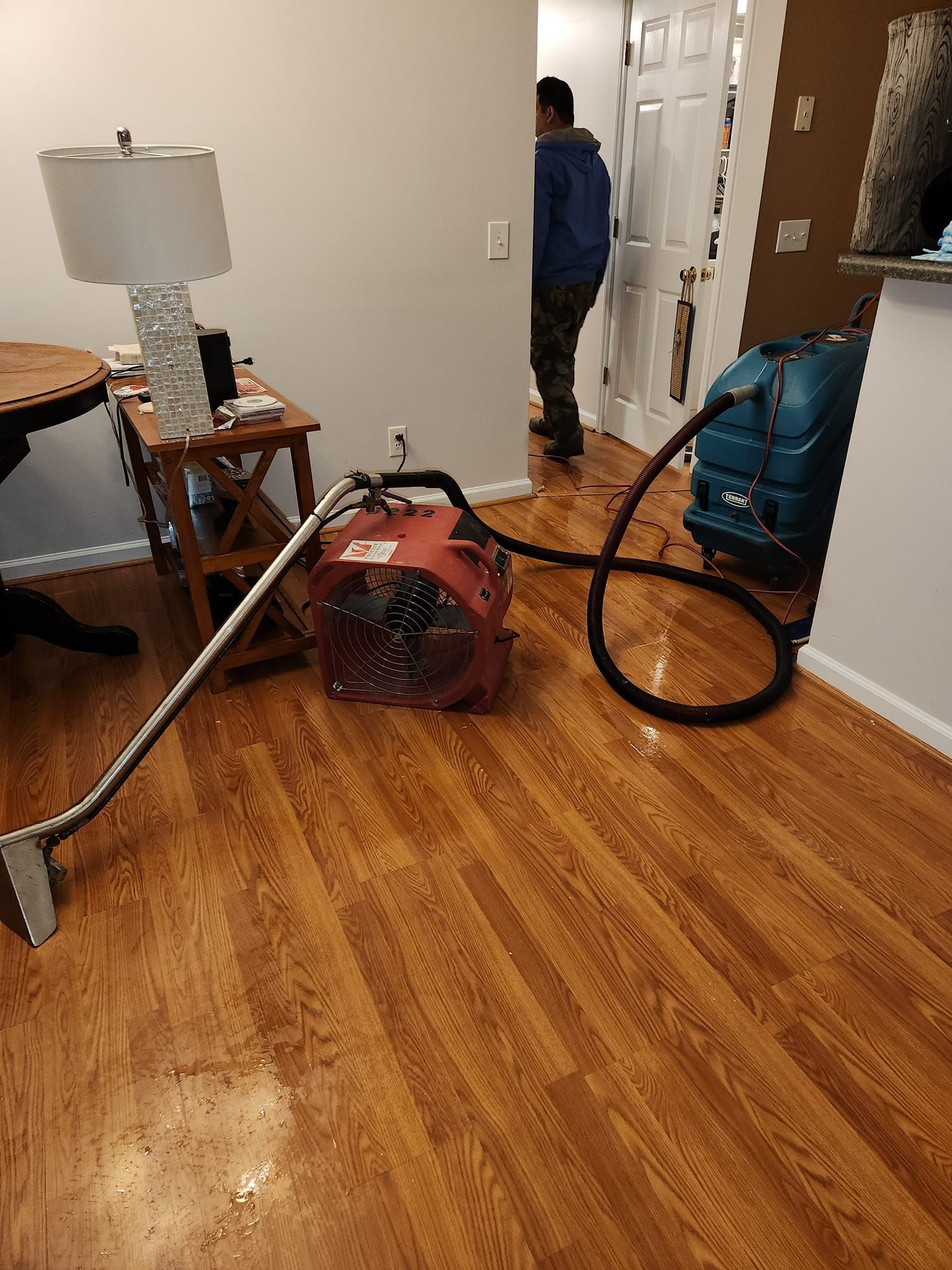 Red fan and hose on wood floor, person in doorway, water extraction equipment.
