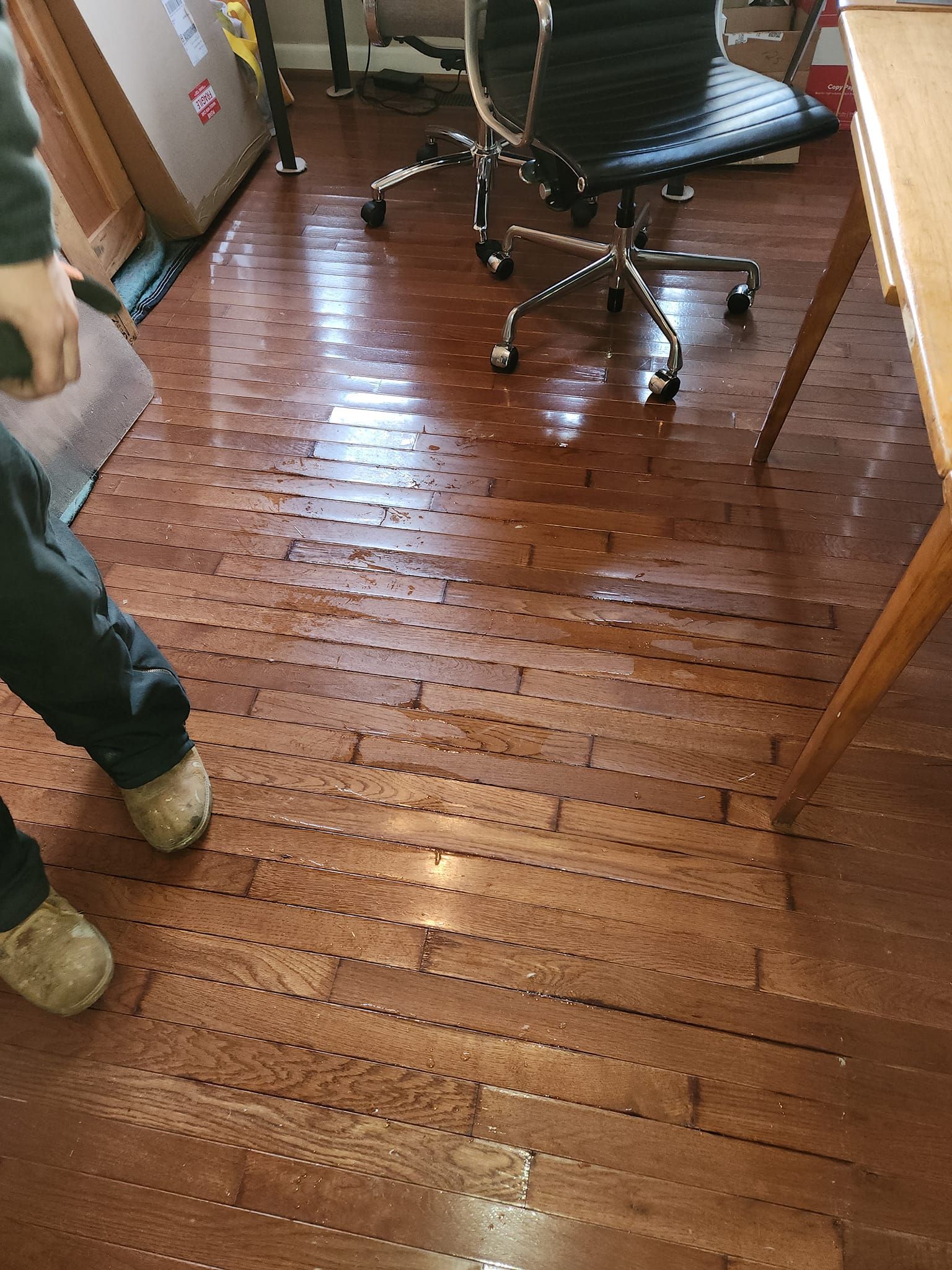 Person standing on wet, damaged hardwood floor, near an office chair and desk.