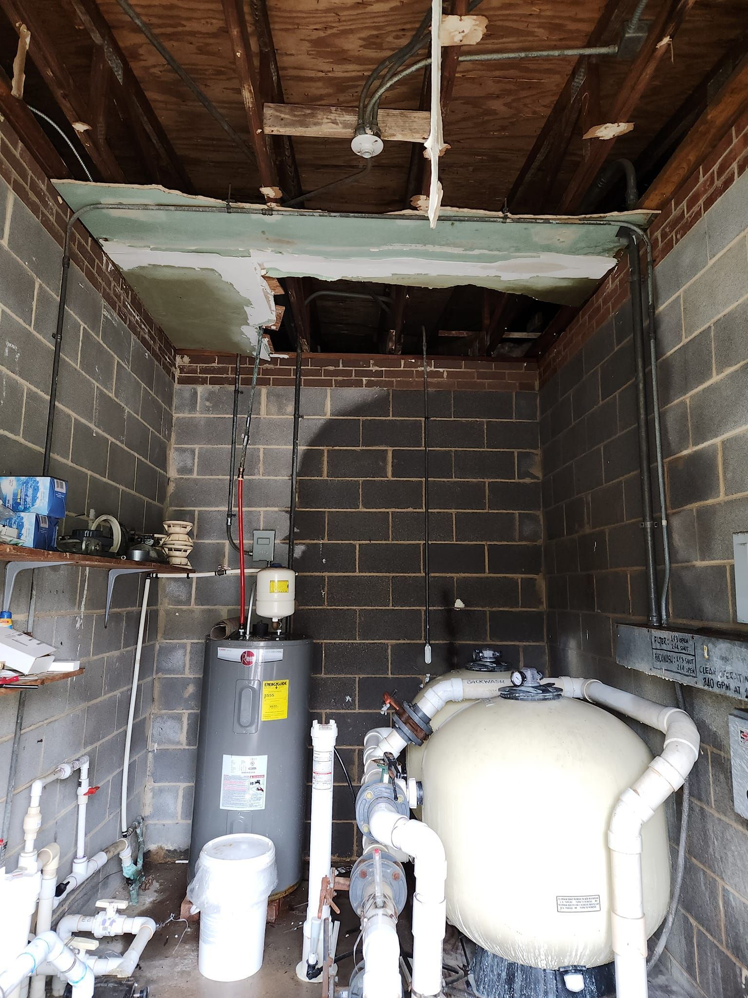 Pool equipment room with damaged ceiling, water heater, filter, and exposed wiring.
