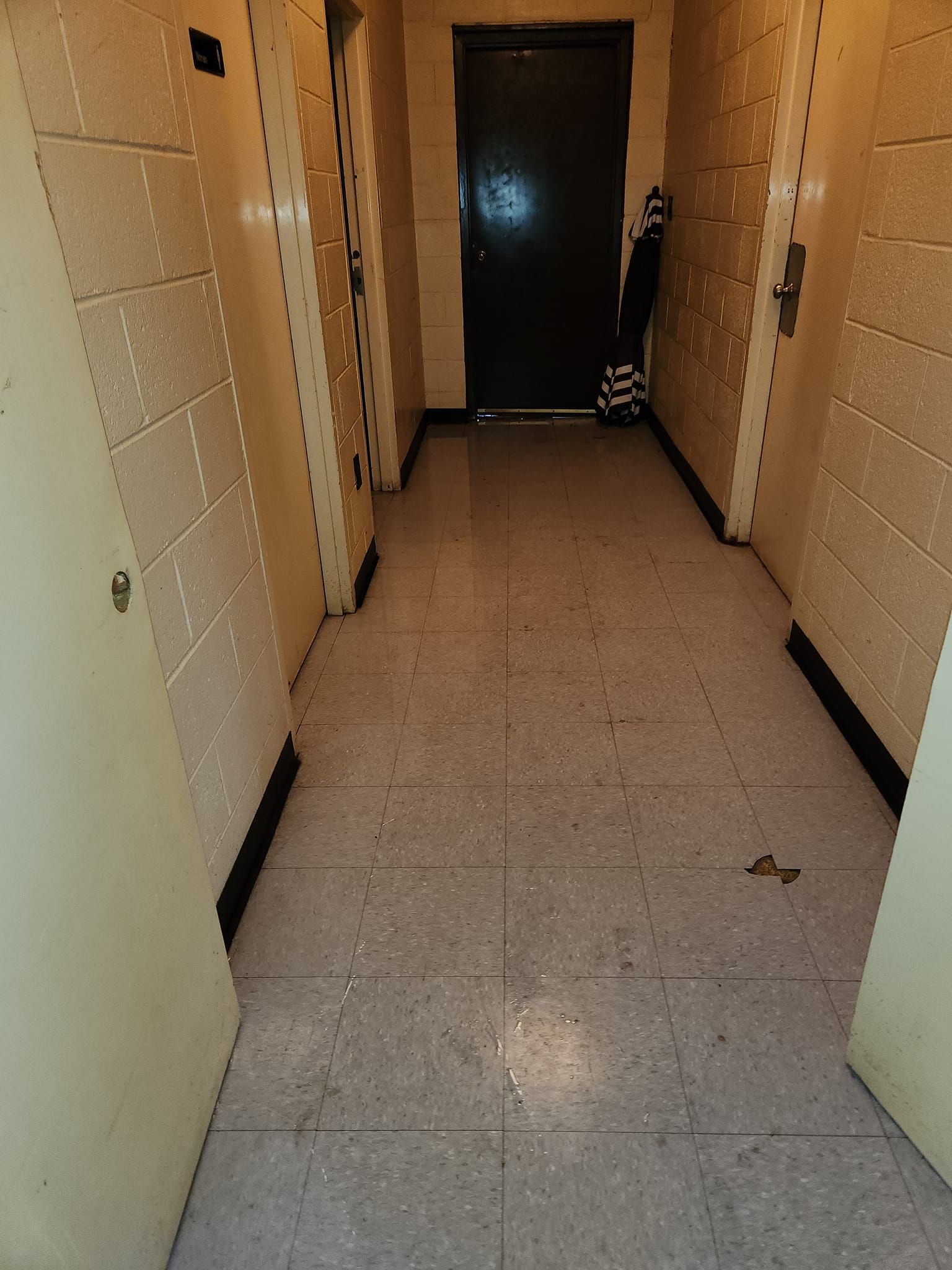 Hallway with closed doors, off-white walls, speckled floor, dark door at the end.