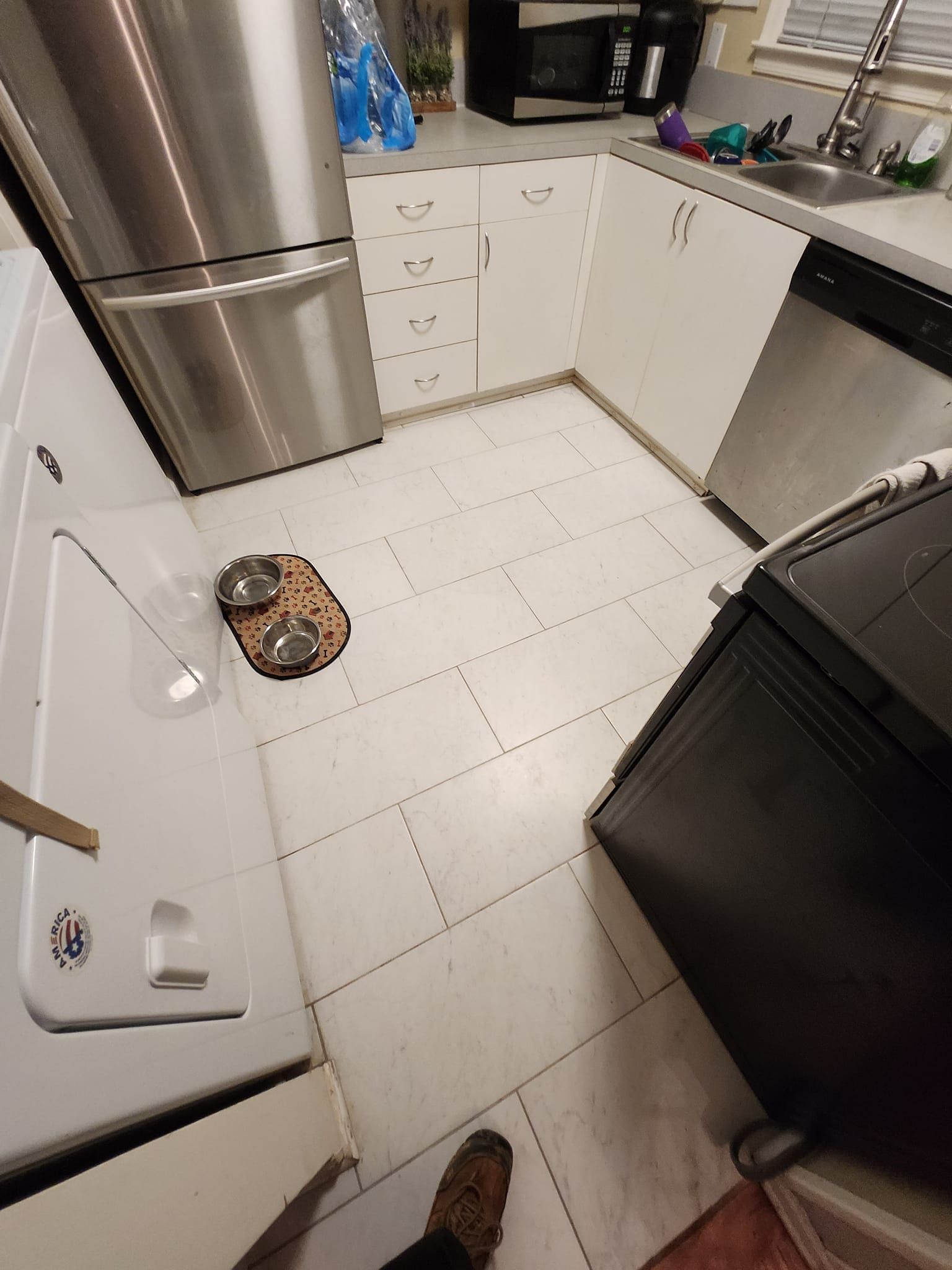 Kitchen with stainless steel appliances, white cabinets, and white tile floor. Includes a stove, sink, and fridge.