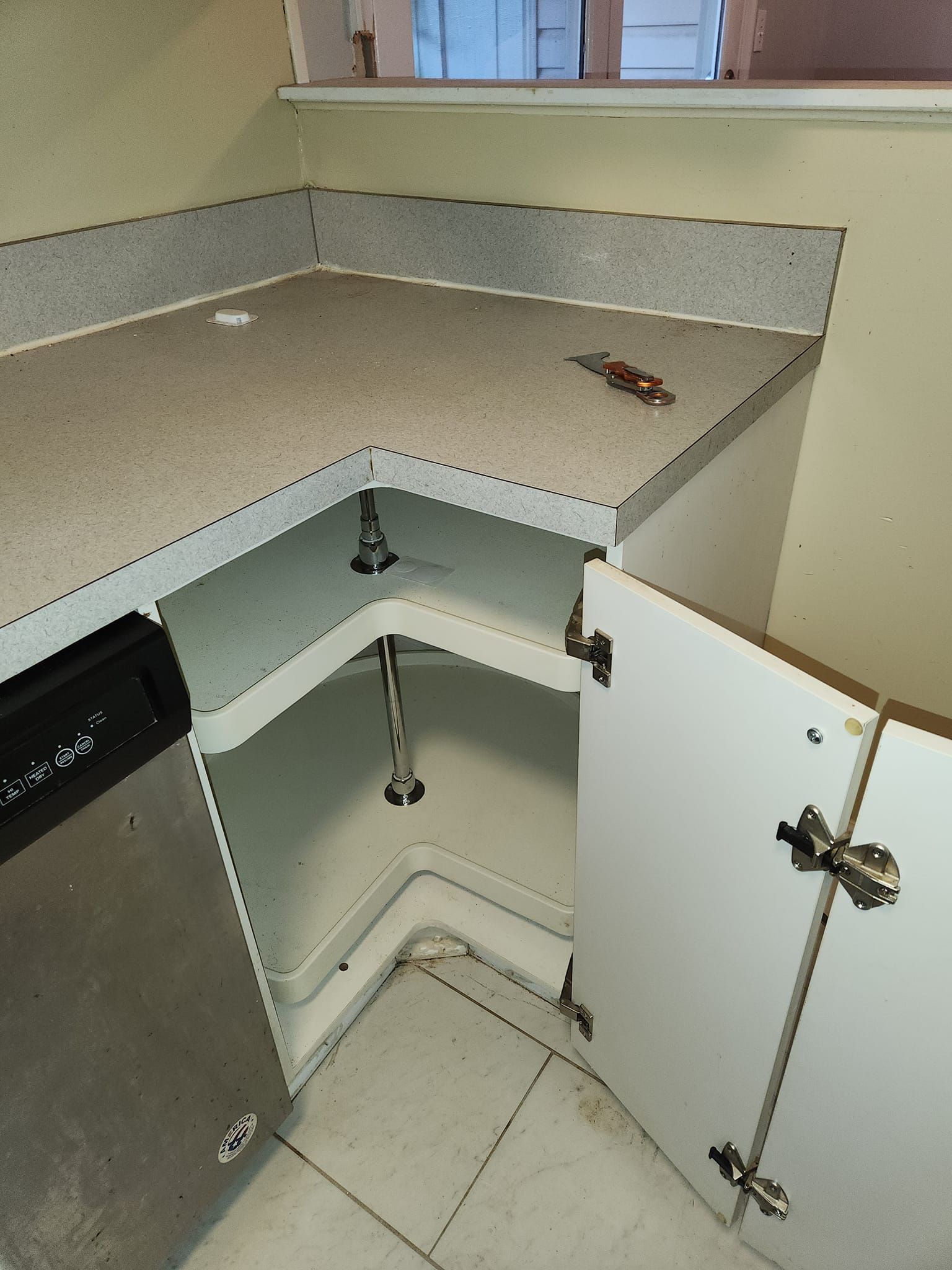 Kitchen cabinet corner with open door, countertop, and plumbing visible.