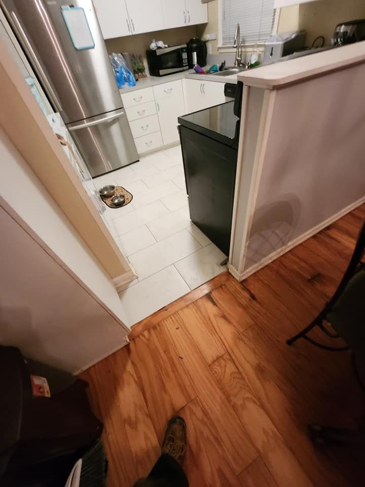 Kitchen doorway; stainless steel fridge, white cabinets, black stove. Brown wood floor, white tile in kitchen.