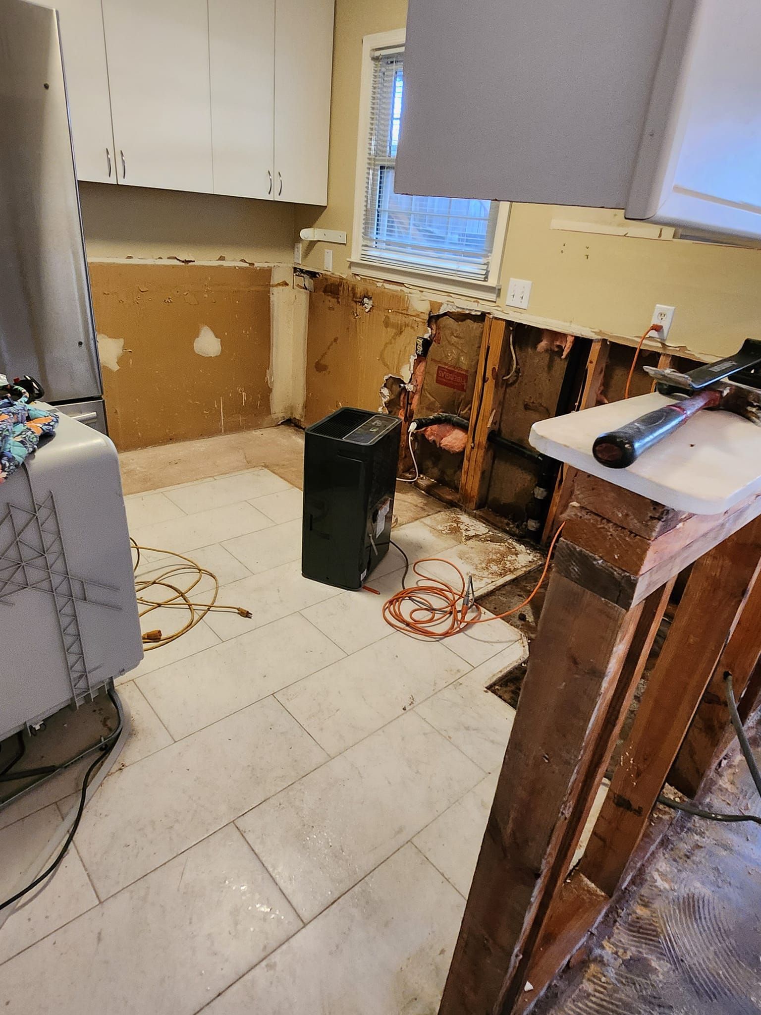 Kitchen undergoing renovation; cabinets removed, walls exposed, construction debris visible.