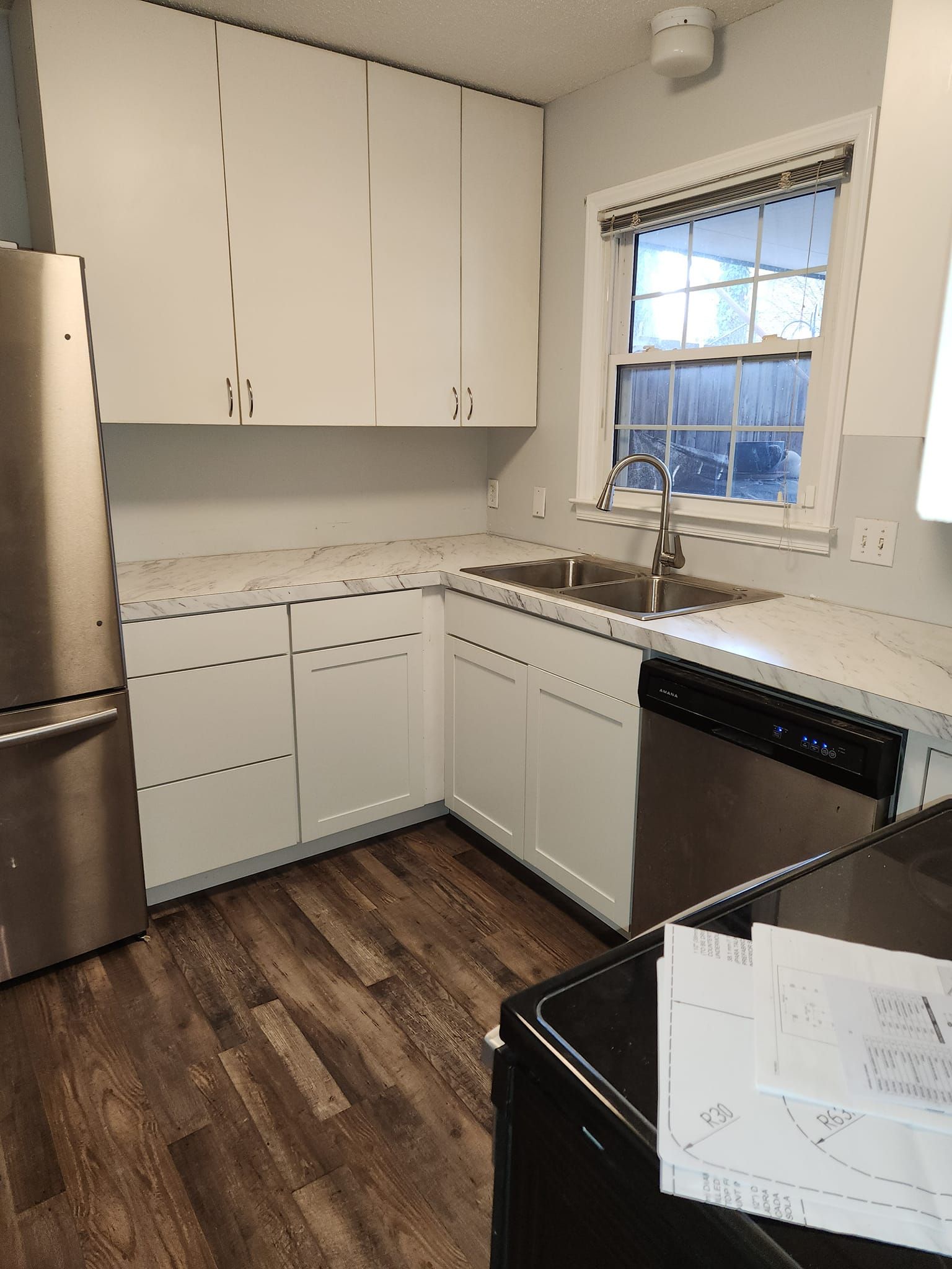 White kitchen cabinets, countertop, and appliances; stainless steel refrigerator; sink under a window.